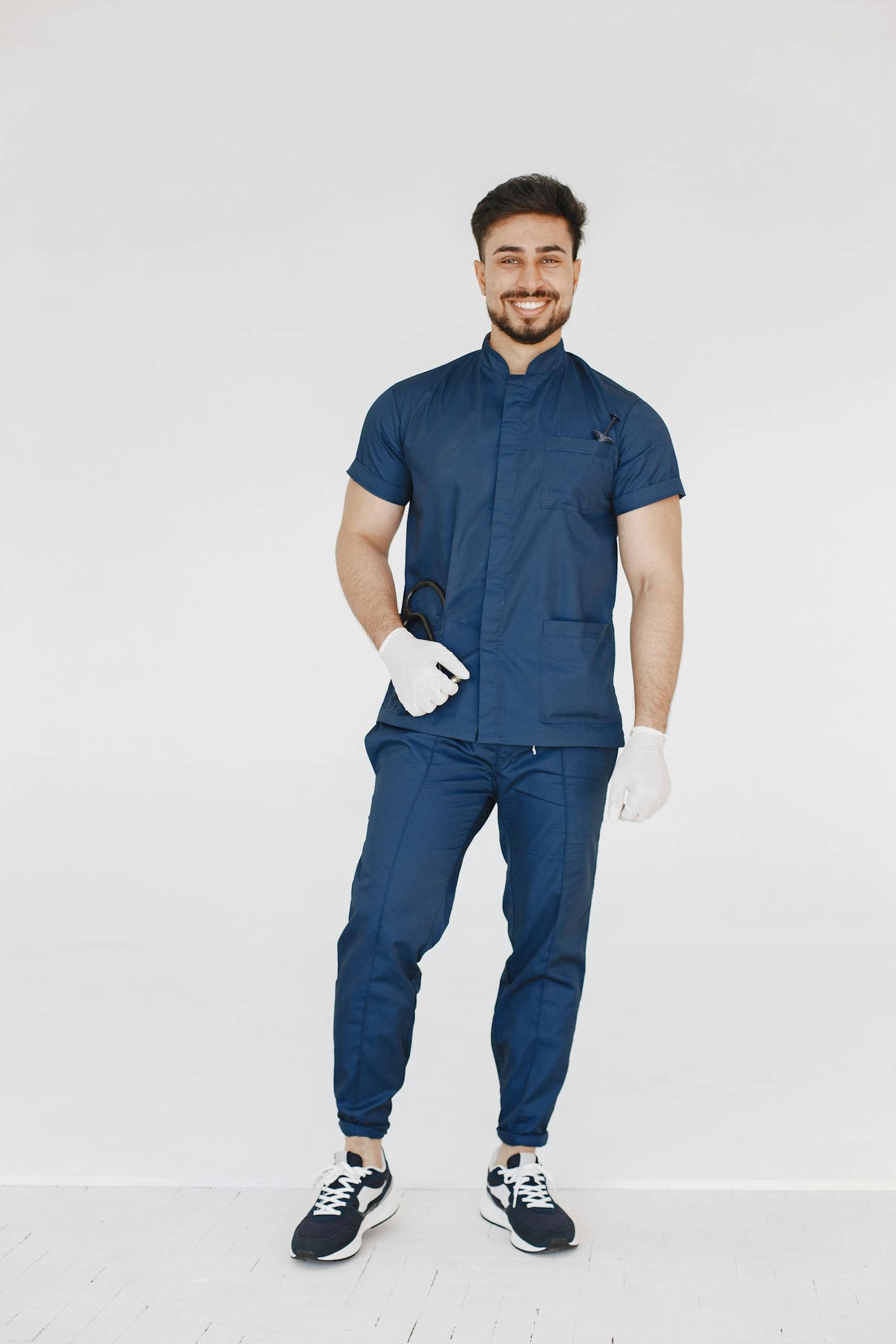 Smiling male doctor in blue medical uniform poses joyfully in a studio setting.